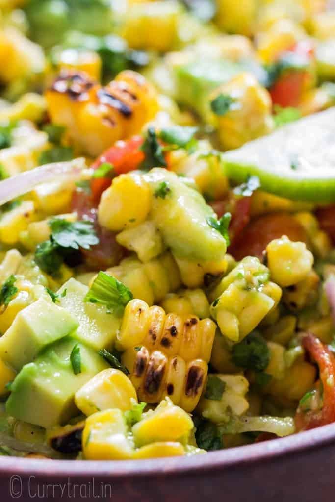 avocado corn tomato salad in wooden salad bowl with lime wedges