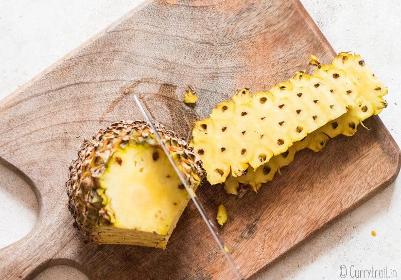 cutting though skin on pineapple on wooden board