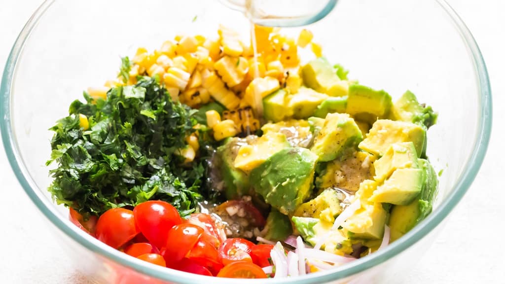 pouring salad dressing over the bowl of salad.