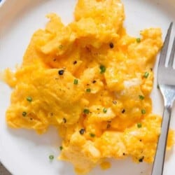 creamy moist scrambled eggs in white plate with fork