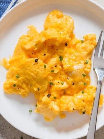 creamy moist scrambled eggs in white plate with fork