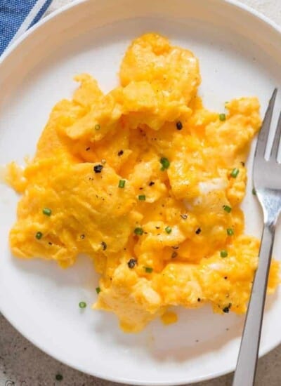 creamy moist scrambled eggs in white plate with fork