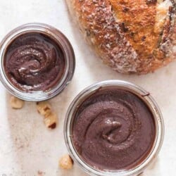 healthy homemade Nutella in two glass jars with sour dough bread loaf on side