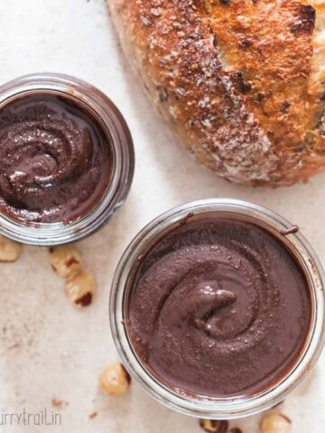 healthy homemade Nutella in two glass jars with sour dough bread loaf on side