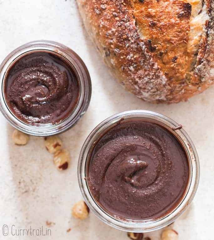 healthy homemade Nutella in two glass jars with sour dough bread loaf on side