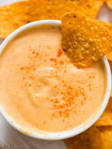 spicy nacho cheddar cheese sauce in small bowl with nachos on side