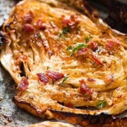 Cabbage steaks roasted in the oven and garnished with Parmesan and bacon on a baking tray.