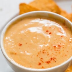 close up view of spicy cheese sauce in a bowl with nachos.