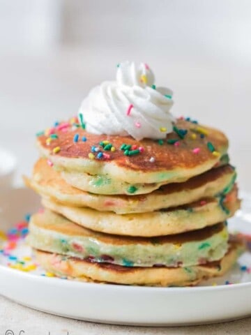 birthday cake pancakes on white plate with whipped cream and sprinkles