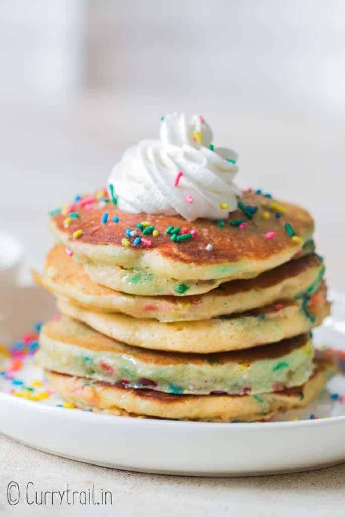 birthday cake pancakes on white plate with whipped cream and sprinkles