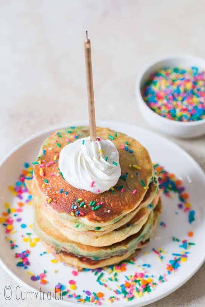 birthday cake pancakes on white plate with whipped cream and sprinkles