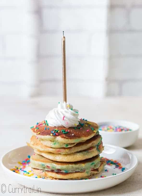 birthday cake pancakes on white plate with whipped cream and sprinkles