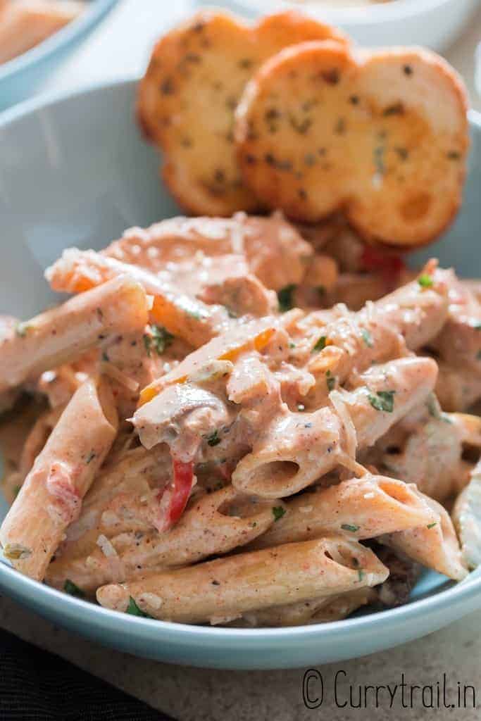 chicken pasta with cajun seasoning in cream sauce served in bowl with garlic bread on sides