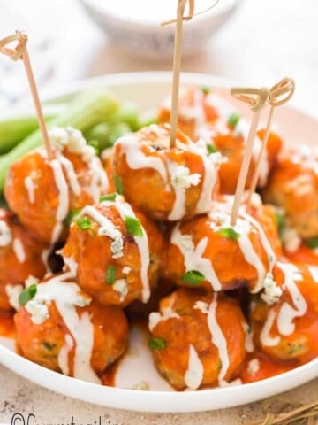 buffalo chicken meatballs stacked up on plate with blue cheese dressing on side