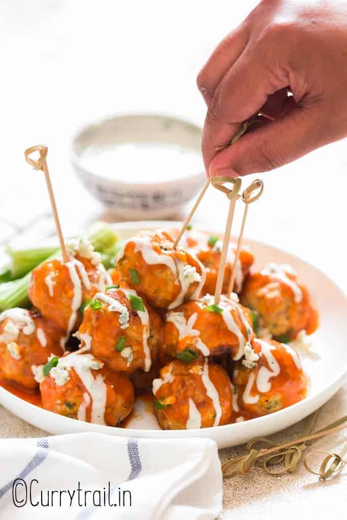 buffalo chicken meatballs stacked up on plate with blue cheese dressing on side with text
