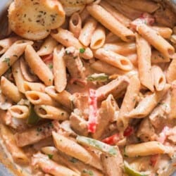 chicken pasta with cajun seasoning in cream sauce served in skillet with bread on sides