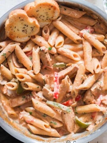 chicken pasta with cajun seasoning in cream sauce served in skillet with bread on sides