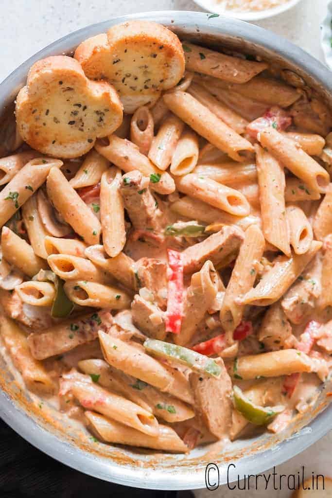 chicken pasta with cajun seasoning in cream sauce served in skillet with bread on sides
