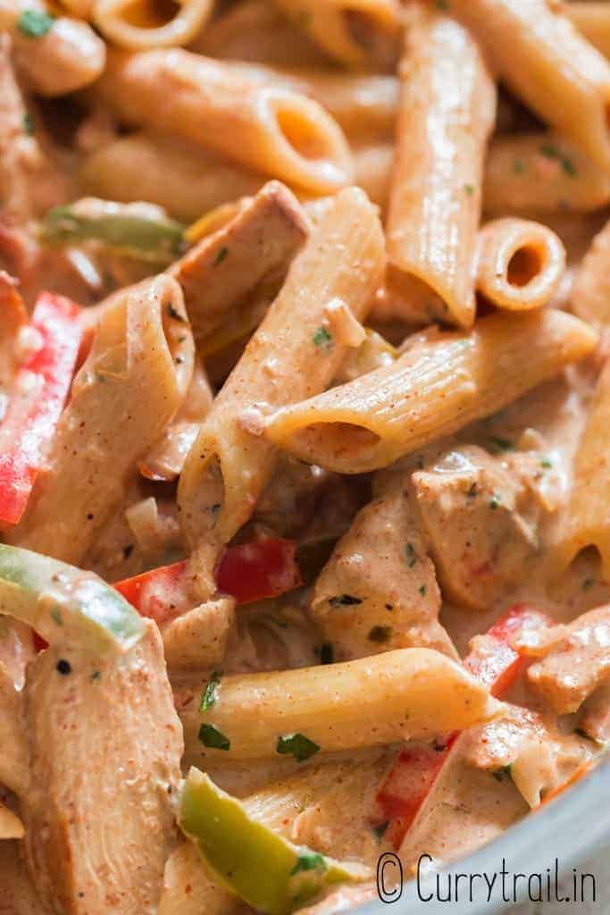 close up of chicken pasta with cajun seasoning in cream sauce served in skillet with bread on sides