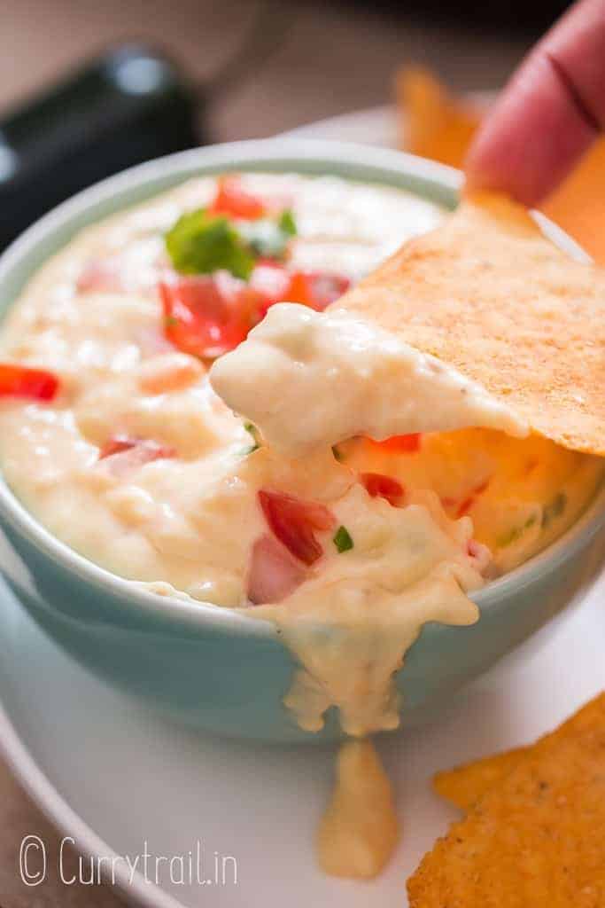 bowl full of white queso dip garnsih with fresh pico de gallo with nachos on side