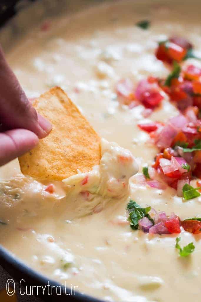 nacho dipped in warm white queso dip cooked in cast iron pan