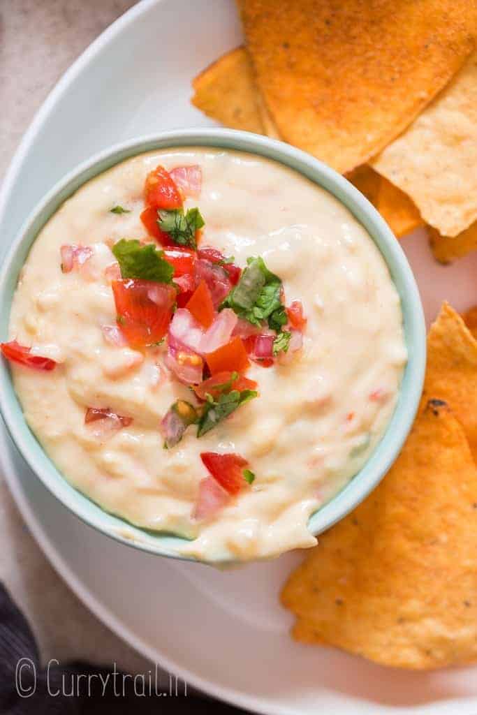 bowl full of white queso dip garnsih with fresh pico de gallo with nachos on side