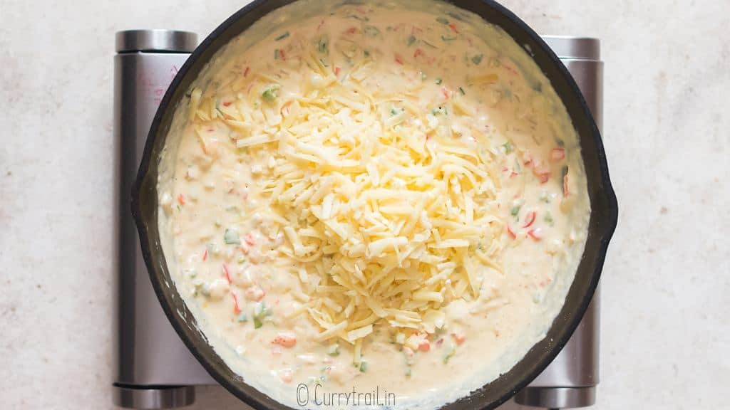 adding freshly grated cheese to white queso dip in skillet.