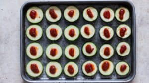 adding topping on zucchini slices for making pizza bites