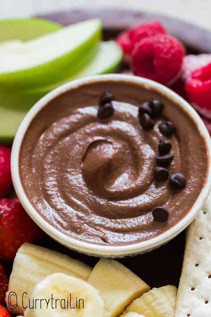 brownie batter hummus in ceramic bowl with fruits and crackers on the side