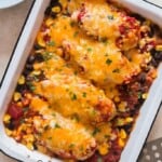 chicken breasts baked with corn, beans, and tomatoes and topped with cheese in a casserole dish.