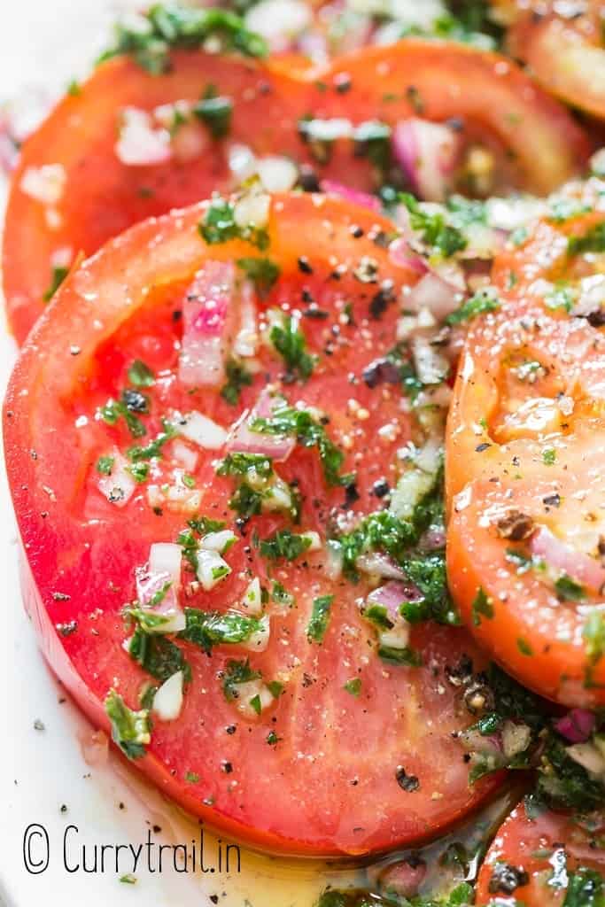 close up of tomatoes marinated in olive oil and herbs on plate