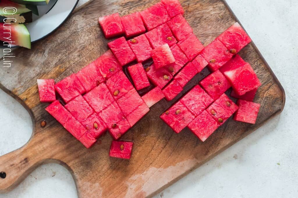 watermelon cut into cubes on wooden board.