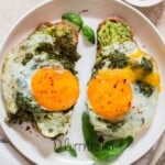 sunny side egg cooked with pesto sauce served on a bread toast.