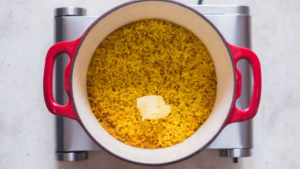 butter is added to fluffy long-grain turmeric rice in a pot.