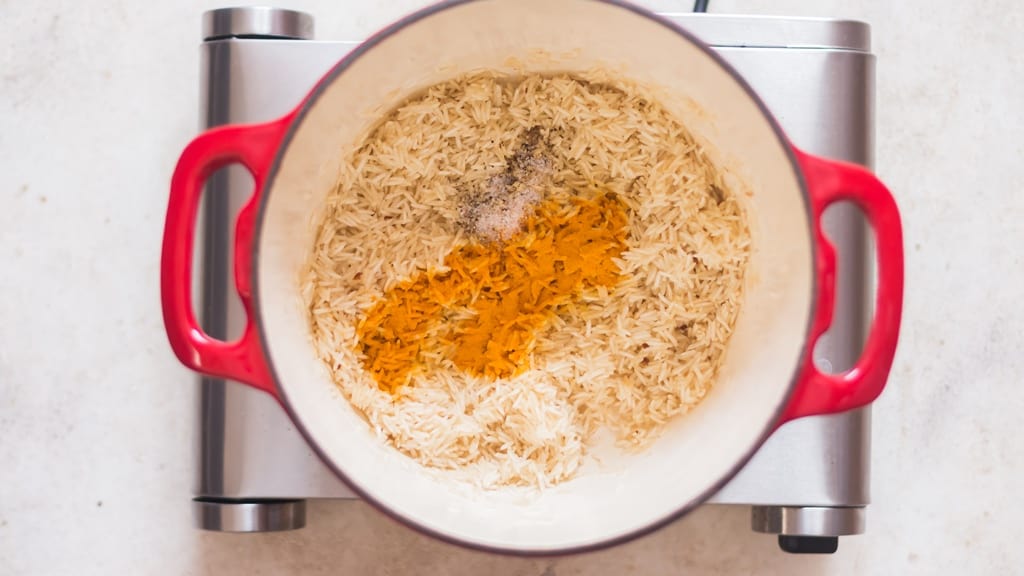 turmeric powder is added to long-grain grain for turmeric rice in a pot.