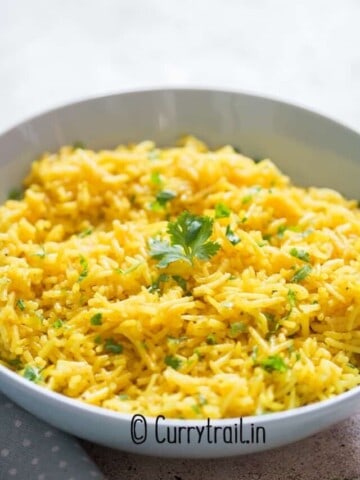 yellow turmeric rice in a bowl garnished with parsley.