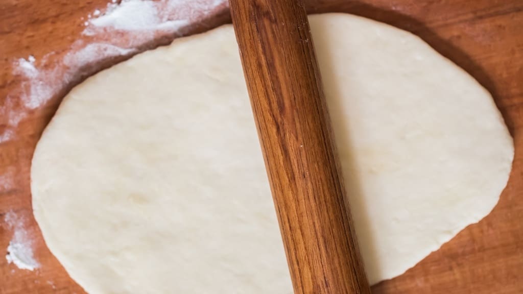 rolling dough with a rolling pin on a wooden surface.