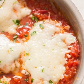 close up view of chicken breast covered in mozzarella cheese cooked in skillet