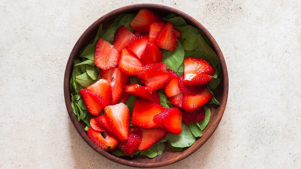 all ingredients for spinach strawberry salad in a wooden salad bowl.