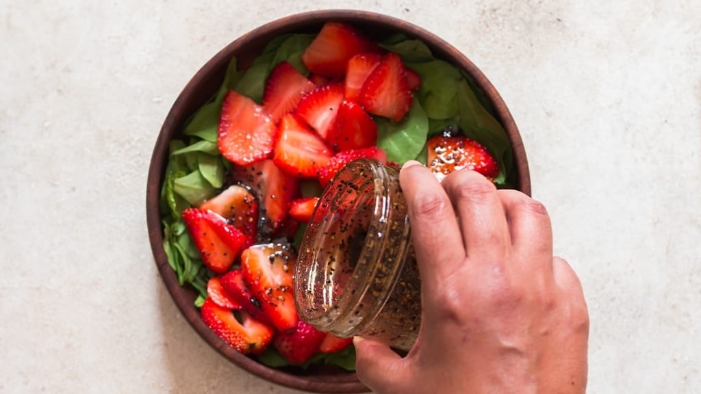 pouring salad dressing over the salad in a bowl.