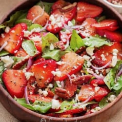 close up view of spinach and strawberry salad in a wooden bowl.