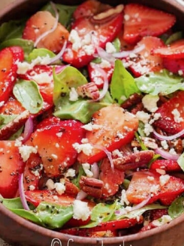 close up view of spinach and strawberry salad in a wooden bowl.