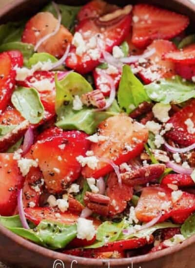 close up view of spinach and strawberry salad in a wooden bowl.