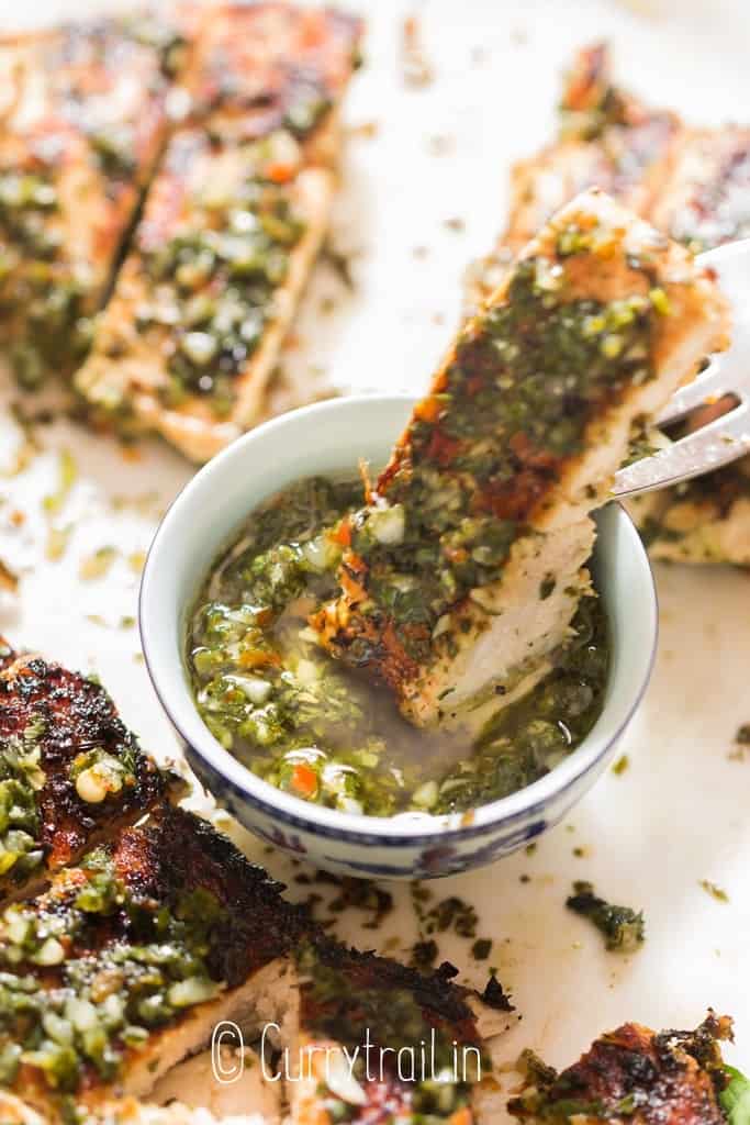 dipping grilled chicken in chimichurri sauce