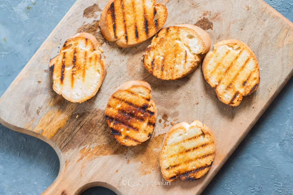 grilled French baguette bread slices on a wooden board.