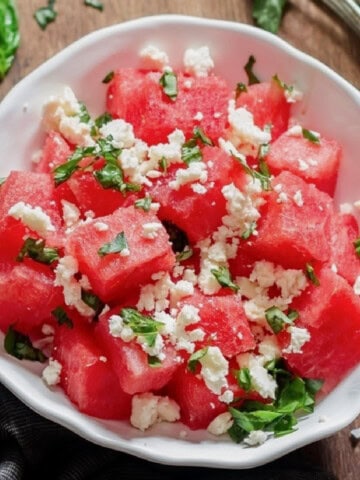 Watermelon and feta salad with basil leaves served in a white bowl.