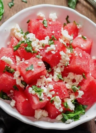 Watermelon and feta salad with basil leaves served in a white bowl.