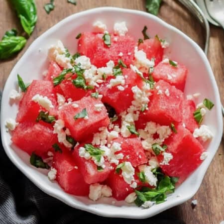 Watermelon and feta salad with basil leaves served in a white bowl.