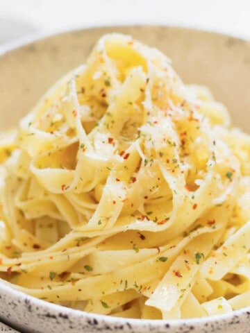 bowl of buttered noodles with herbs and chili flakes seasoning.