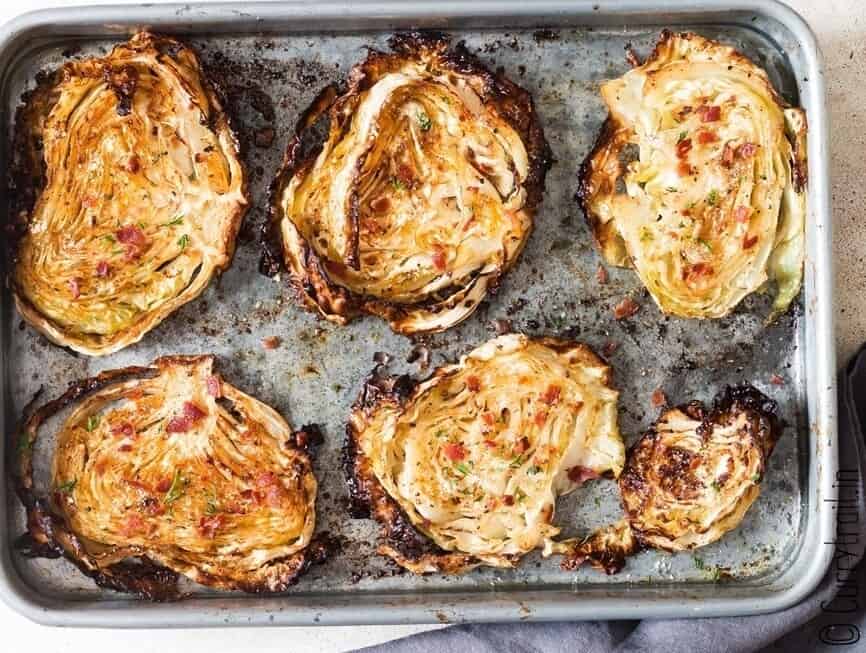 crispy steaks of cabbage roasted in a baking tray with bacon on top.